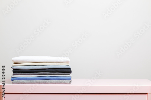 On a pink table is a stack of folded clothes. Gray background. Close-up