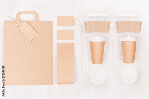 Coffee takeaway set mockup for brand - two brown paper cups with blank bag, card, label, packet, sugar, cap on white wood board, top view.