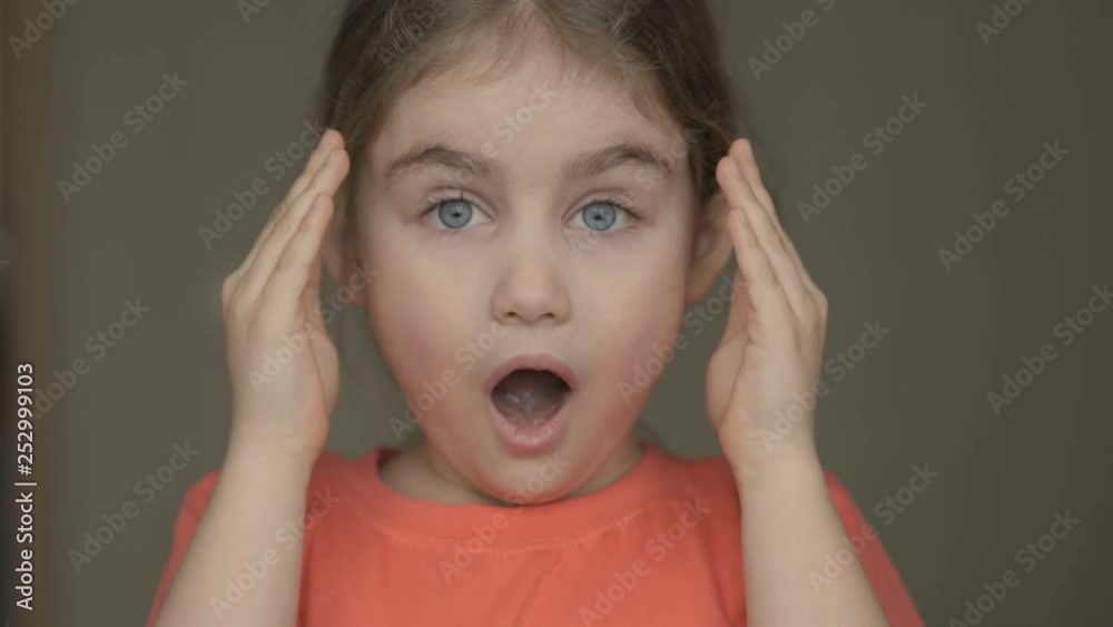 Cute little girl open her face with hands. Girl looks and is surprised and happy to receive a surprise. Portrait little young girl with blue eyes looking at camera. Closeup Cute little girl open her face with hands. Girl looks and is surprised and happy to receive a surprise. Portrait little young girl with blue eyes looking at camera. Closeup