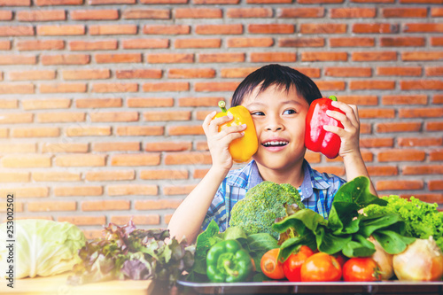 Happiness boy holding colorful sweet peppers with fresh vegetables on table