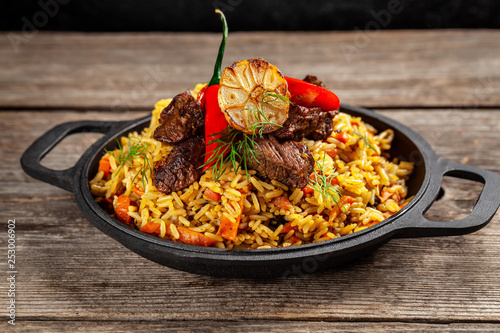 The concept of oriental cuisine. National Uzbek pilaf with meat in a cast-iron skillet, on a wooden table. background image. top view, copy space, flat lay