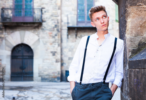 young European guy in shirt and trousers with suspenders walking around city
