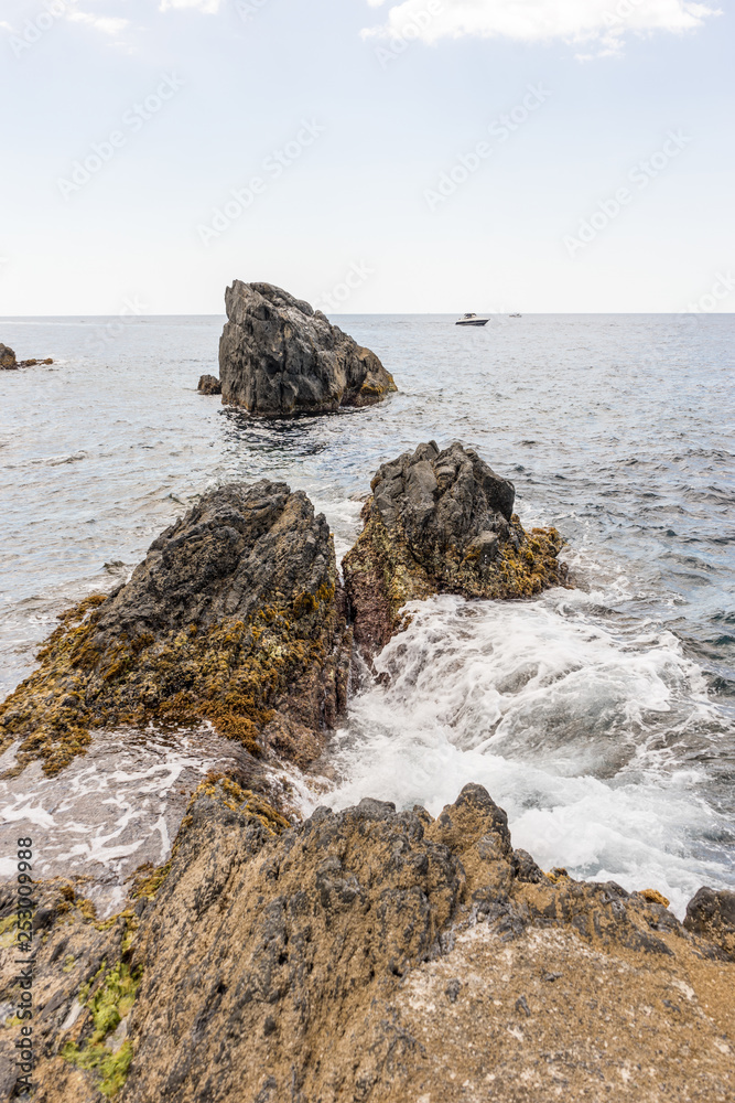 Italy, Cinque Terre, Manarola, a person sitting on a rock next to a body of water