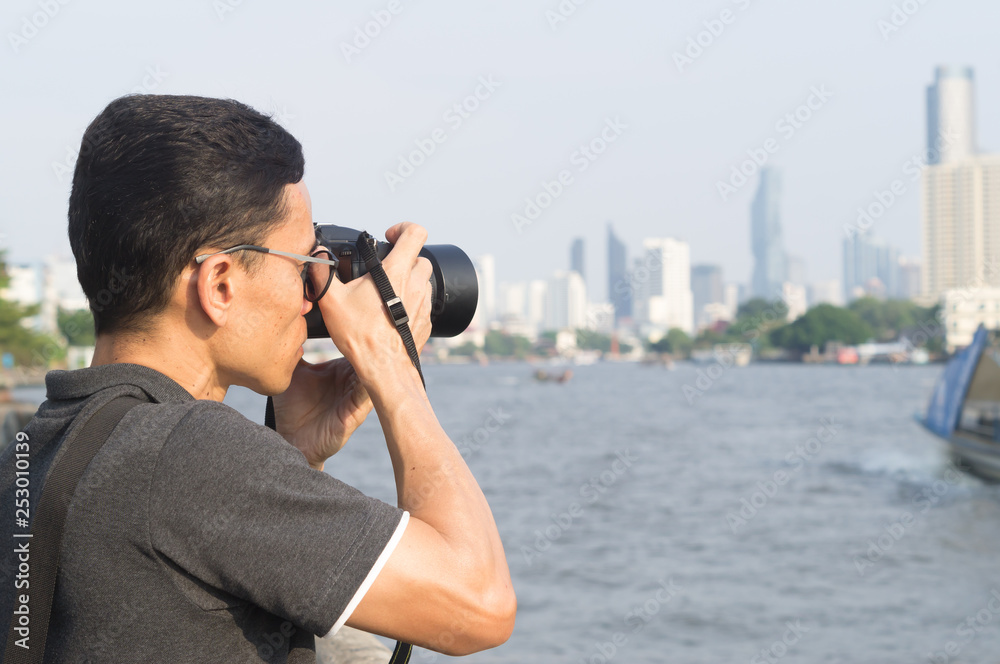 A man taking photos at the river with surrounding tall buildings and tree in distance