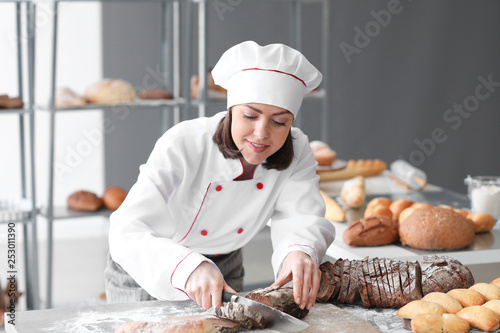 Female baker cutting fresh bread in kitchen