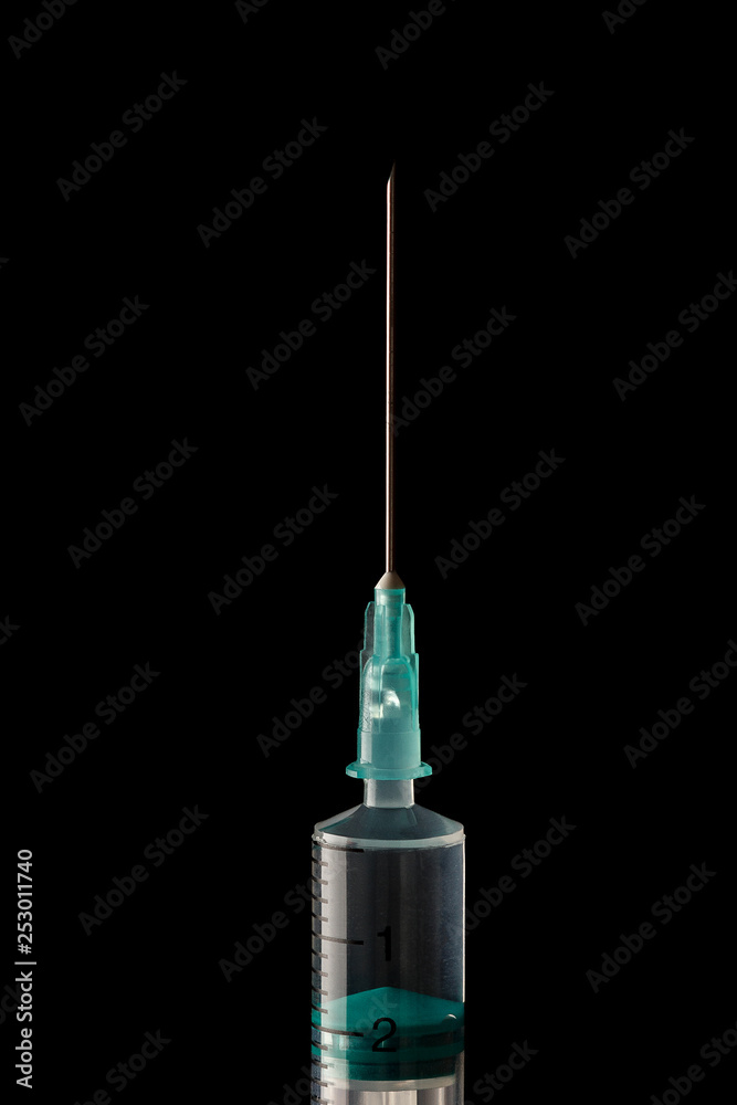 The end of the syringe with a needle filled with liquid on a dark background. The end of the syringe with a needle filled with liquid on a dark background.