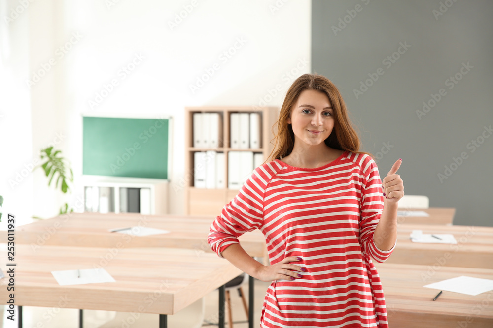 Cute schoolgirl showing thumb-up in classroom