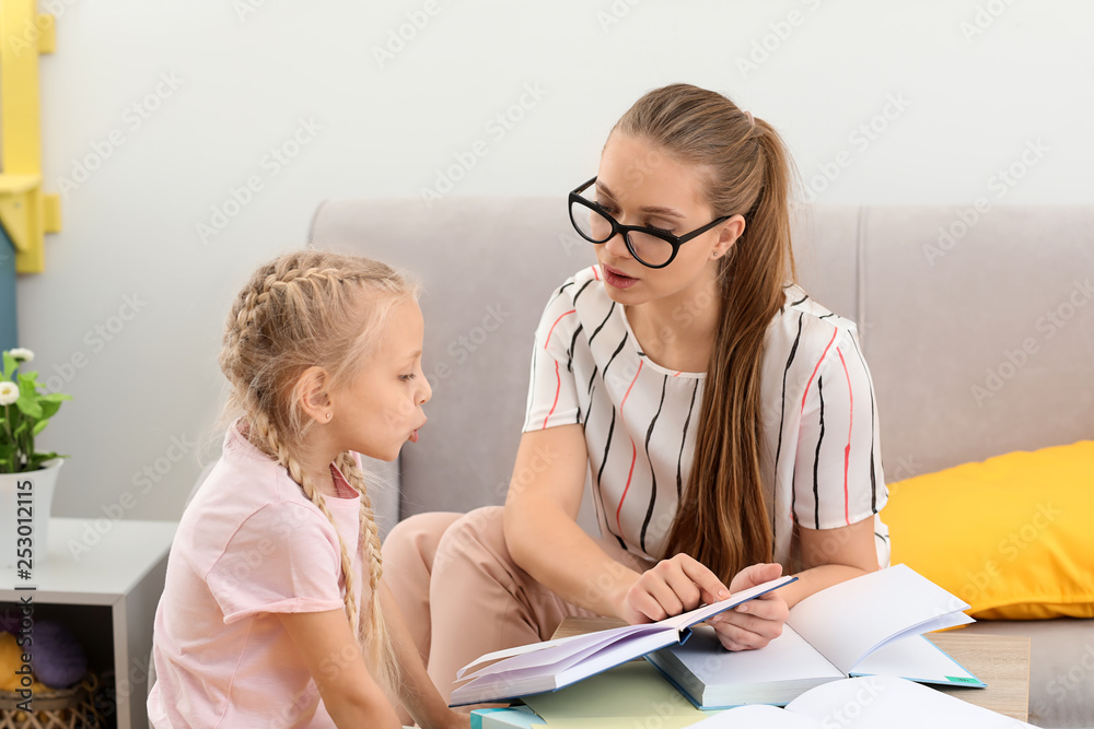 Little girl with speech therapist reading book in office