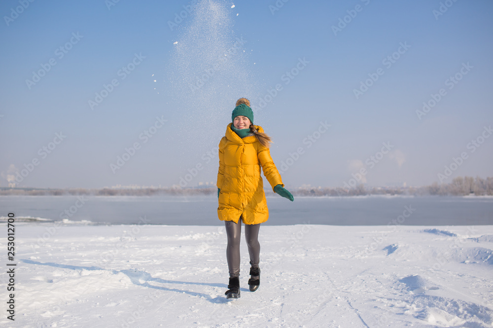 Young woman in yellow down jacket walks and smiles outside