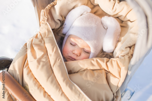 Little baby in cap of hare sleeps in baby carriage outside
