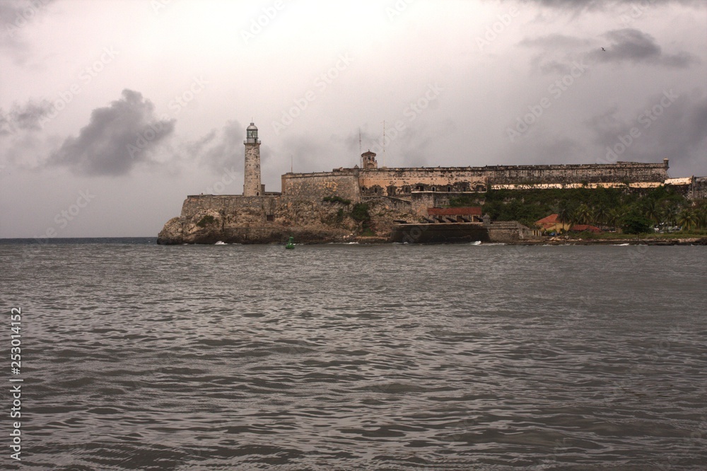 Stone lighthouse and fortress on water with background of cloudy sky