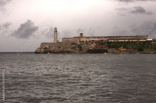 Stone lighthouse and fortress on water with background of cloudy sky © Andrew