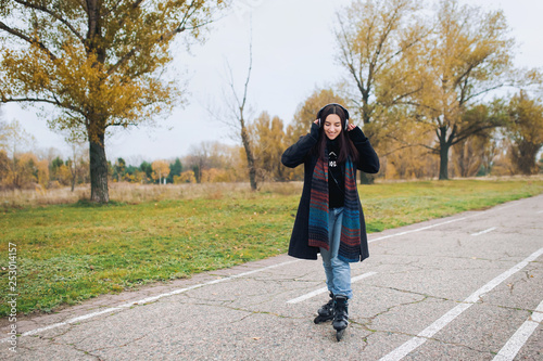 Young beautiful smiling girl in casual wear roller skating listens to music. Autumn walk in the fresh air.