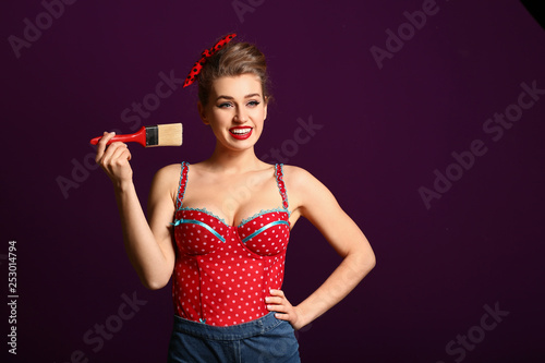 Beautiful pin-up woman with paint brush on color background