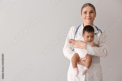 Pediatrician with African-American baby on light background
