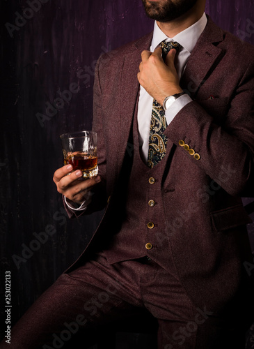 the man in the suit straightens his tie around his neck, in the hands of whiskey