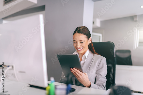 Gorgeous brunette with big toothy smile dressed in formal wear sitting in office and using tablet for work. Sell the problem you solve, not the product. © dusanpetkovic1