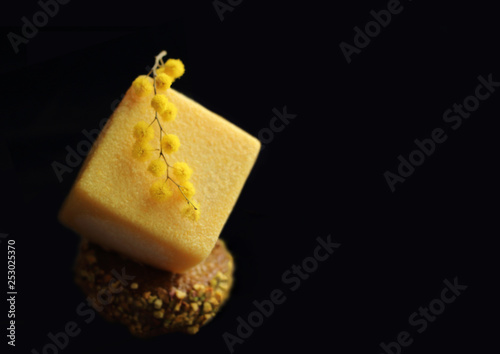 Yellow cube dessert with mimosa flowers on black background