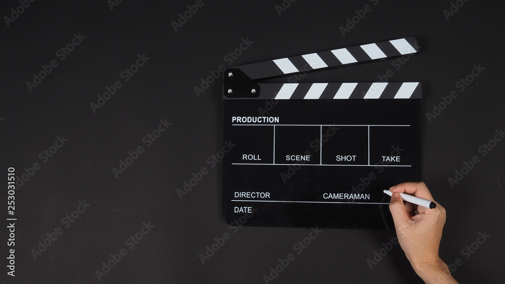 Black Clapperboard or clap board or movie slate use with right hand holding pen in video production ,film, cinema industry on black background.