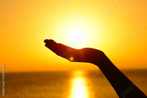 Woman hand holding sun at sunset on the beach