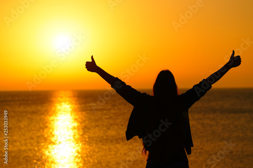 Happy woman with thumbs up celebrating sunrise photo