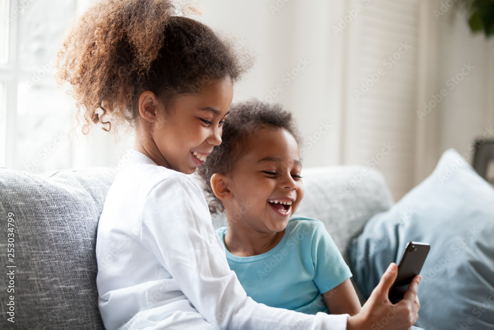 Laughing small black siblings have fun using smartphone Laughing small black siblings have fun using smartphone