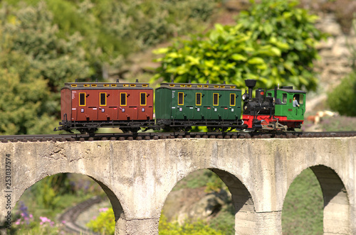 Model of locomotive pushing carriges on a concrete viaduct bridge. Garden model train photo