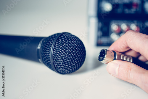 Black microphone holding in hand, and audio cable, mixer in the blurry background