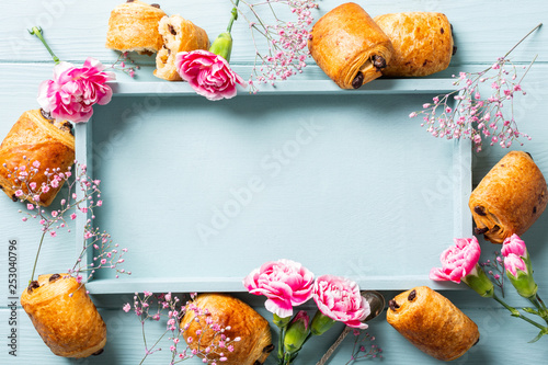 Holiday background with mini fresh croissants bun with chocolate and carnation flowers on blue turquoise background. Top view. Copy space. photo