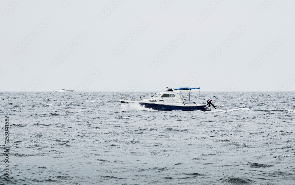 A motorboat floating on the heavy sea with waves in bad weather conditions with other luxury yacht on background.   Boat on the ocean (overcast day) after the storm - image