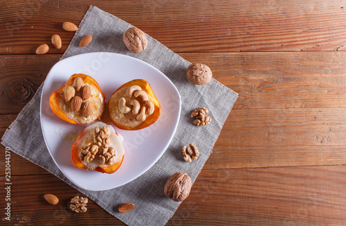 persimmon dessert with curd, nuts and milk cream on brown wooden background.