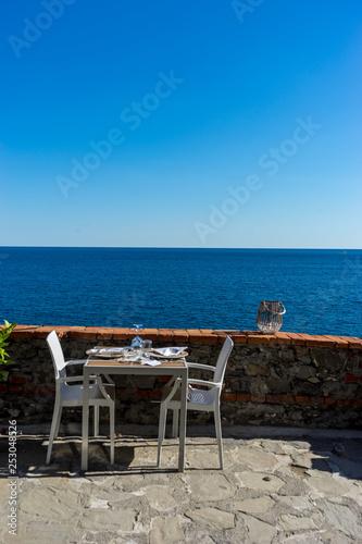 Italy, Cinque Terre, Monterosso, a chair sitting in front of a body of water © SkandaRamana