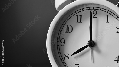 Closeup face of white analog bell clock. Black and white background. Number on clock face.