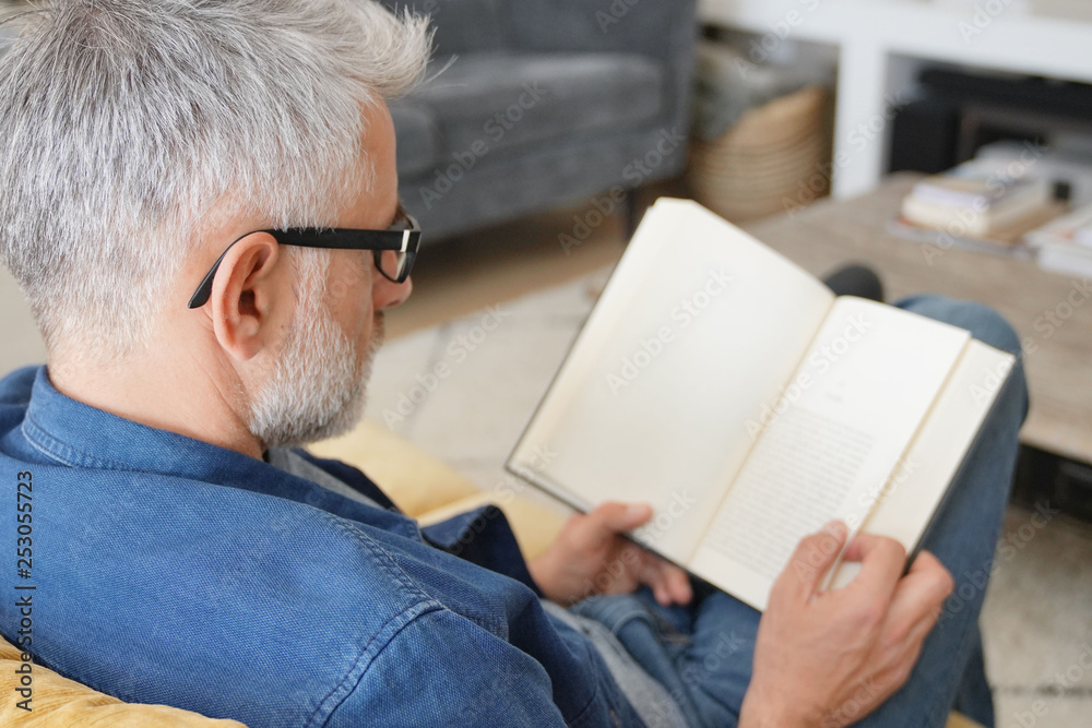 Fototapeta premium Man in 40s reading book in modern home