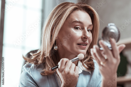 Dark-eyed woman wearing stylish earrings looking into mirror