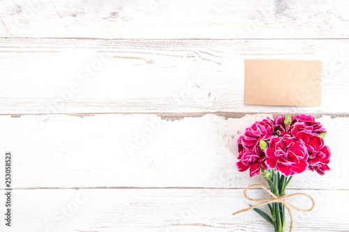 May mothers day concept photography - Beautiful carnations with template card isolated on a bright wooden table, copy space, flat lay, top view, mock up