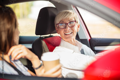 Happy mature business woman driving a car and talking to a young female colleague who is sitting on codriver seat photo