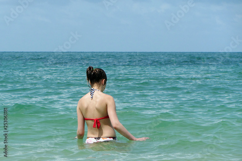 Unrecognizable girl standing in water on tropical ocean beach.