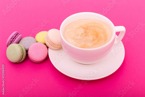Cup of coffee with color macaron on pink background from above, flat lay