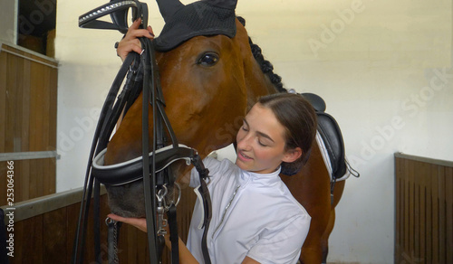 Foto CLOSE UP: Young woman tacking up and putting a bridle on her beautiful horse