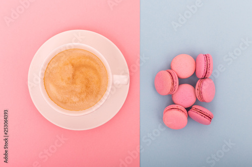 Cup of coffee with macaron on pink and blue background from above, flat lay