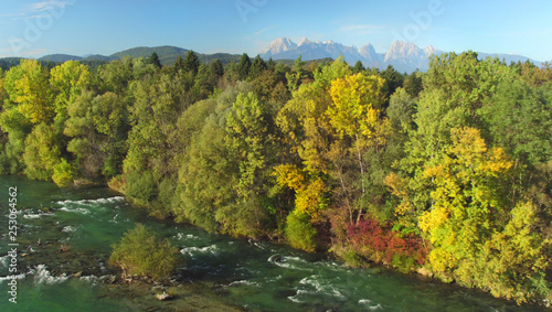 AERIAL Flying over a beautiful blue river flowing past autumn colored forest.