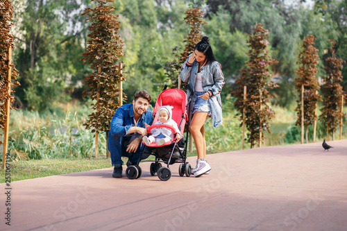 mom and dad are walking in the park with their daughter in a stroller, a beautiful sunny day, a beautiful family © halcon1