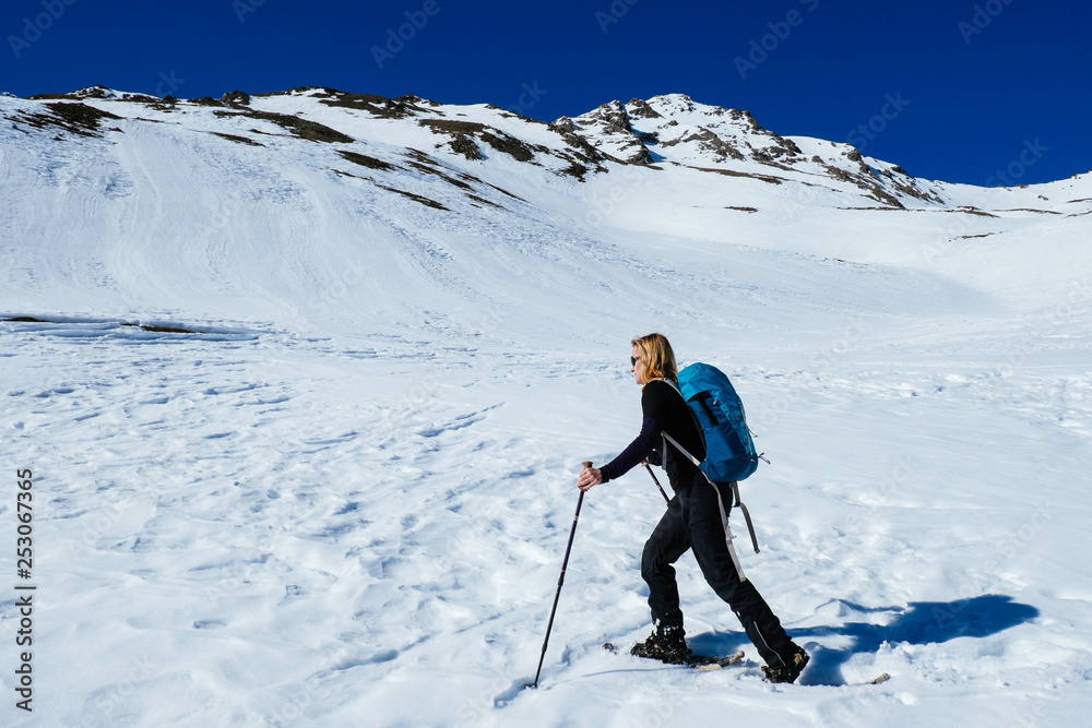 A sporty woman wirh blond hair is walking with snoweshoes the a summit in the alps of italy