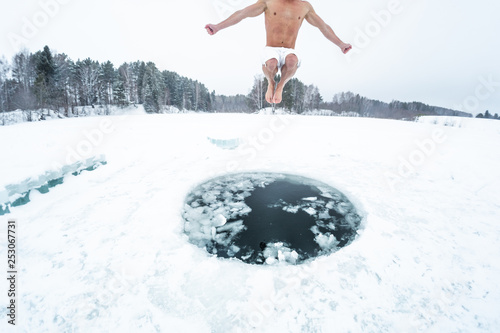 Young man jumps and flies into the ice hole made on the winter lake