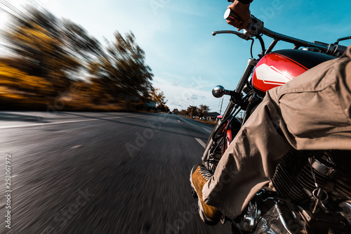 Man rides motorcycle on an empty asphalt road. Blurred trees and road surface.