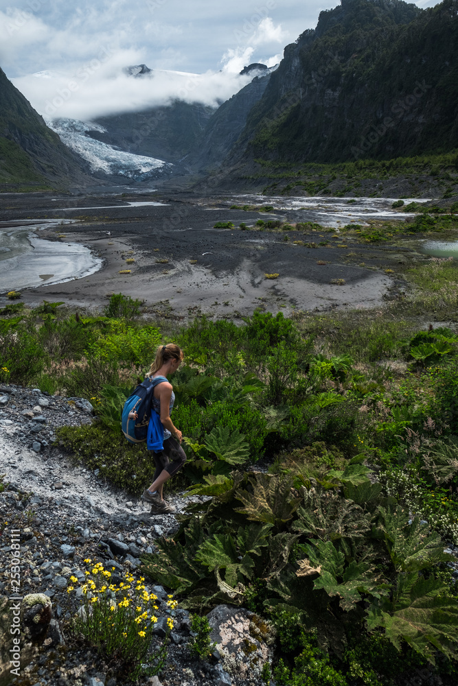 Woman hiker walks in the valley with lush vegetation and glacier on the horizon Woman hiker walks in the valley with lush vegetation and glacier on the horizon