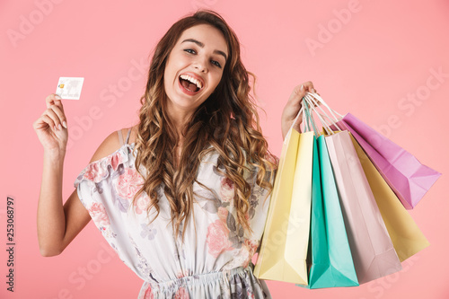 Image of joyful woman 20s in dress holding credit card and colorful shopping bags