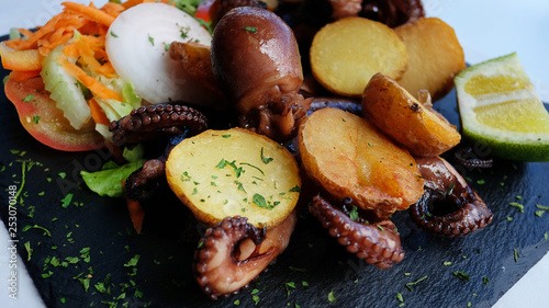 Delicious seafood meal with grilled octopus and baked potatoes and salad served on a black slate appetizer board, a typical Spanish cuisine seafood dish in El Hierro, Canary Islands, Spain
