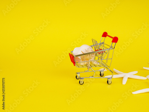 Shopping cart , troley with seashells on yellow background.